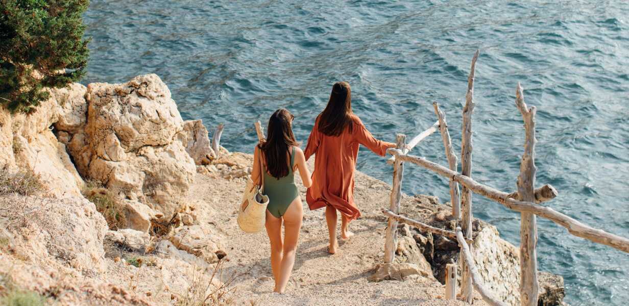 deux jeunes femmes en maillot de bain descendant vers une crique isolee a biza ete