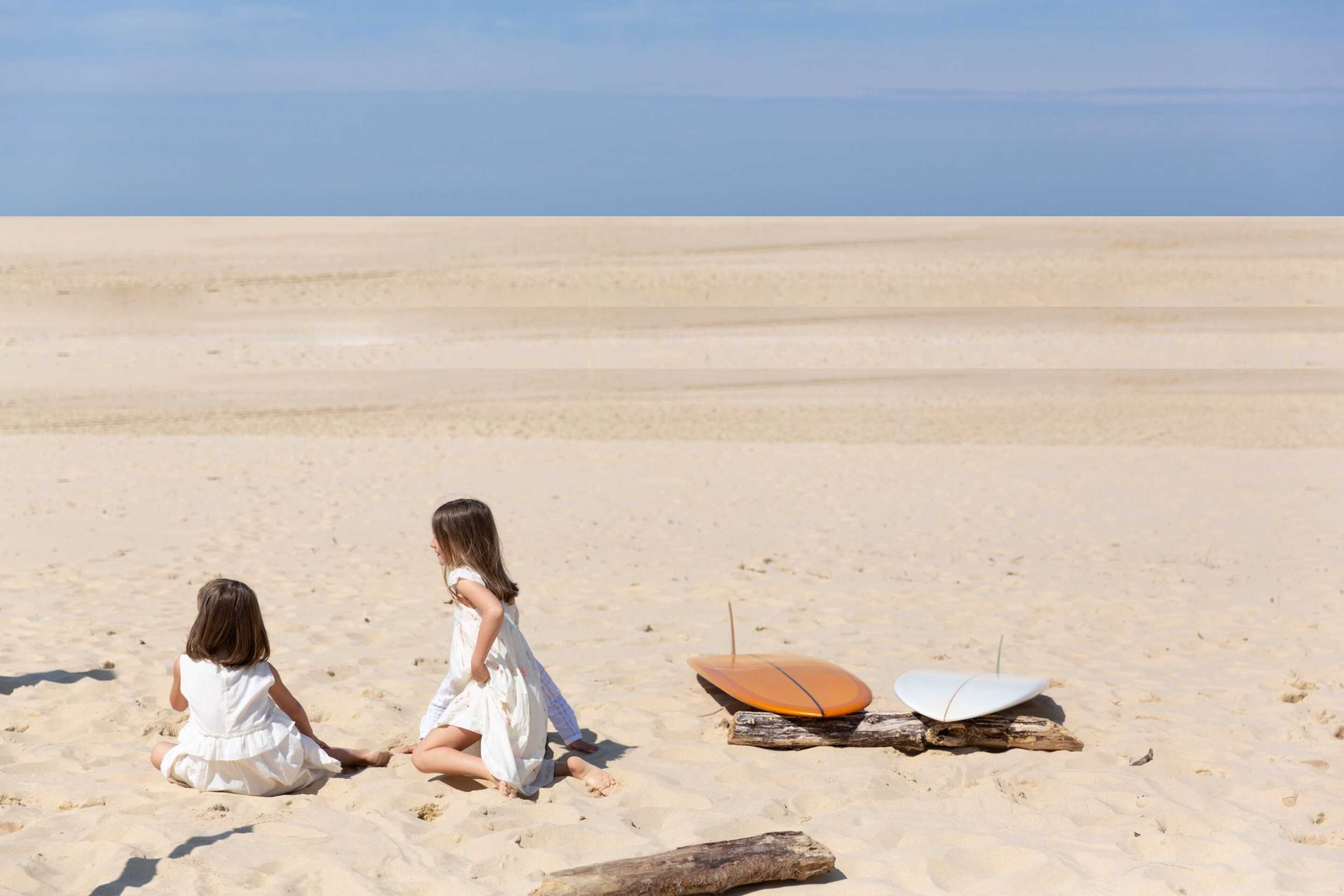 little girls on the beach sitting by a surfboard in the basque country