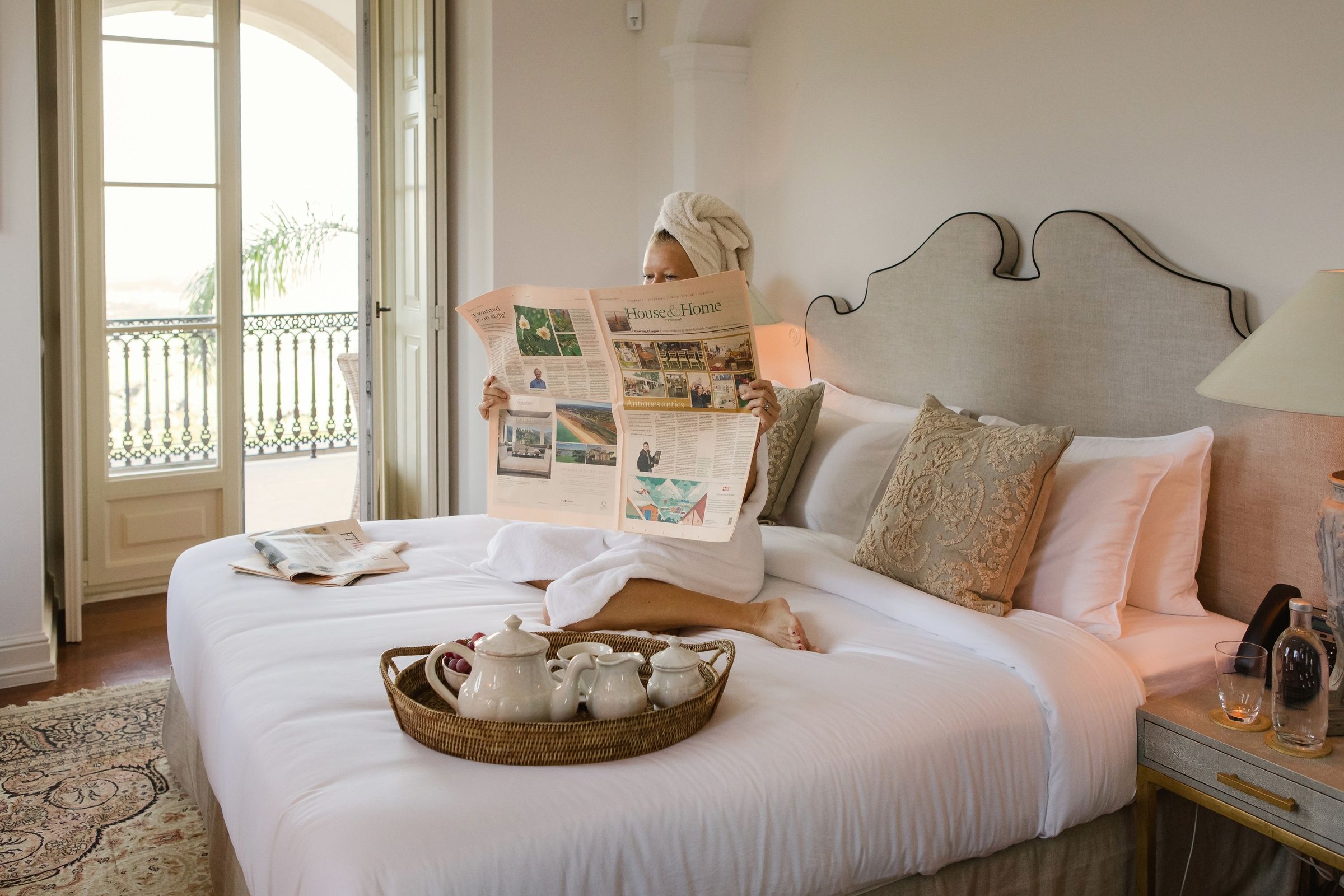 Woman-in-a-dressing-gown-reading-a-newspaper-on-a-bed-with-a-tray-of-tea