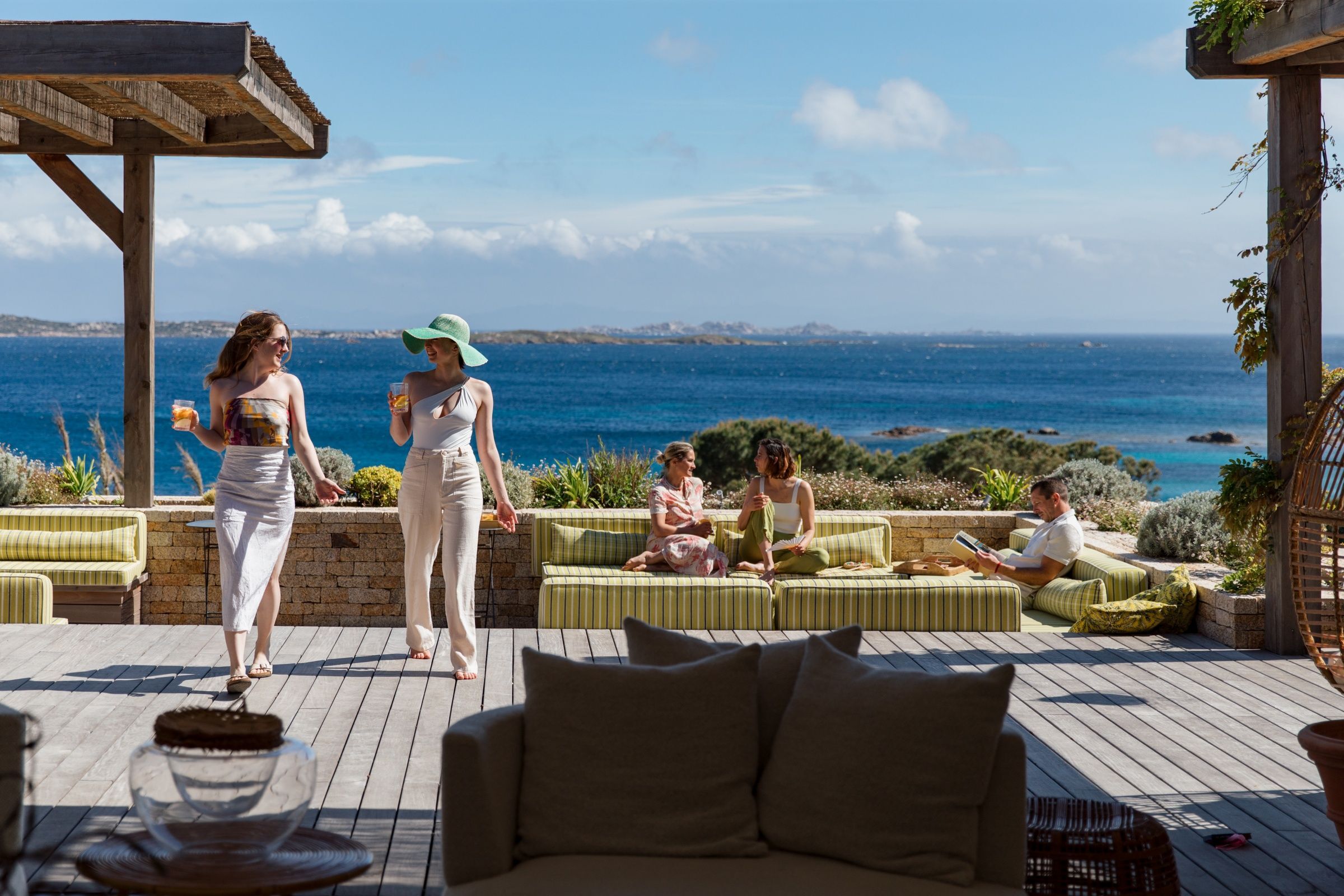 group-of-friends-on-the-wooden-terrace-of-a-luxury-villa-on-an-island-chatting-with-a-panoramic-view-on-the-sea-in-the-background