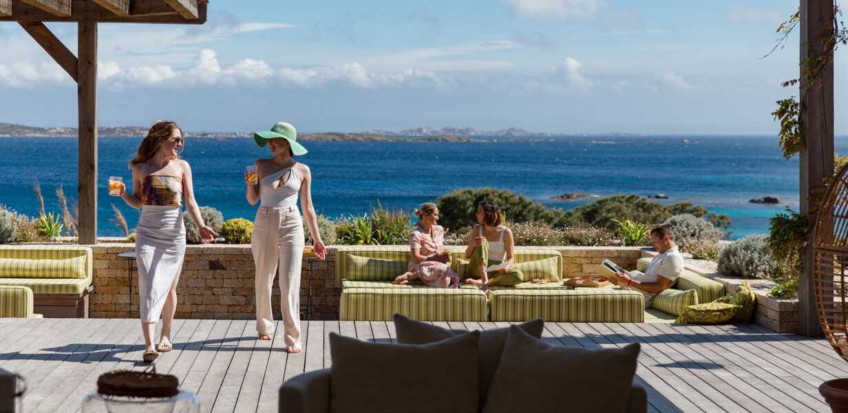 group-of-friends-on-the-wooden-terrace-of-a-luxury-villa-on-an-island-chatting-with-a-panoramic-view-on-the-sea-in-the-background