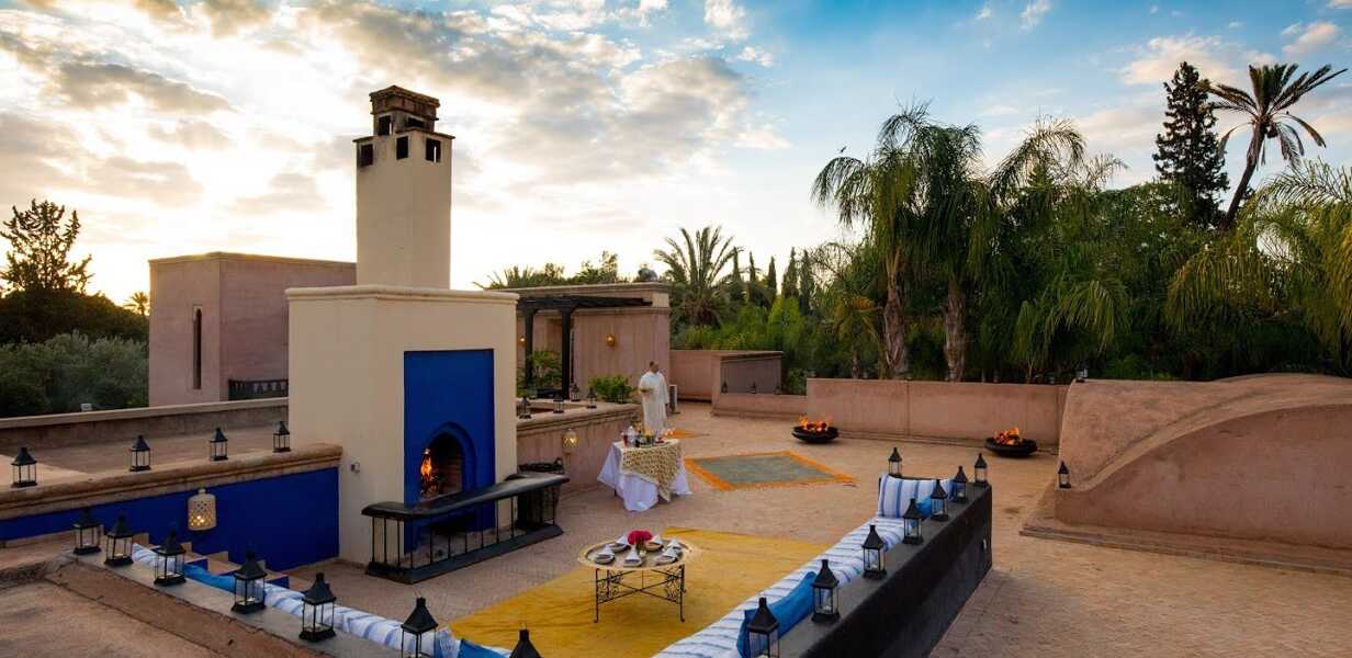 rooftop-d-une-villa-marocaine-avec-des-canapes-et-des-tapis-berberes-une-cheminee-et-des-palmiers-autour