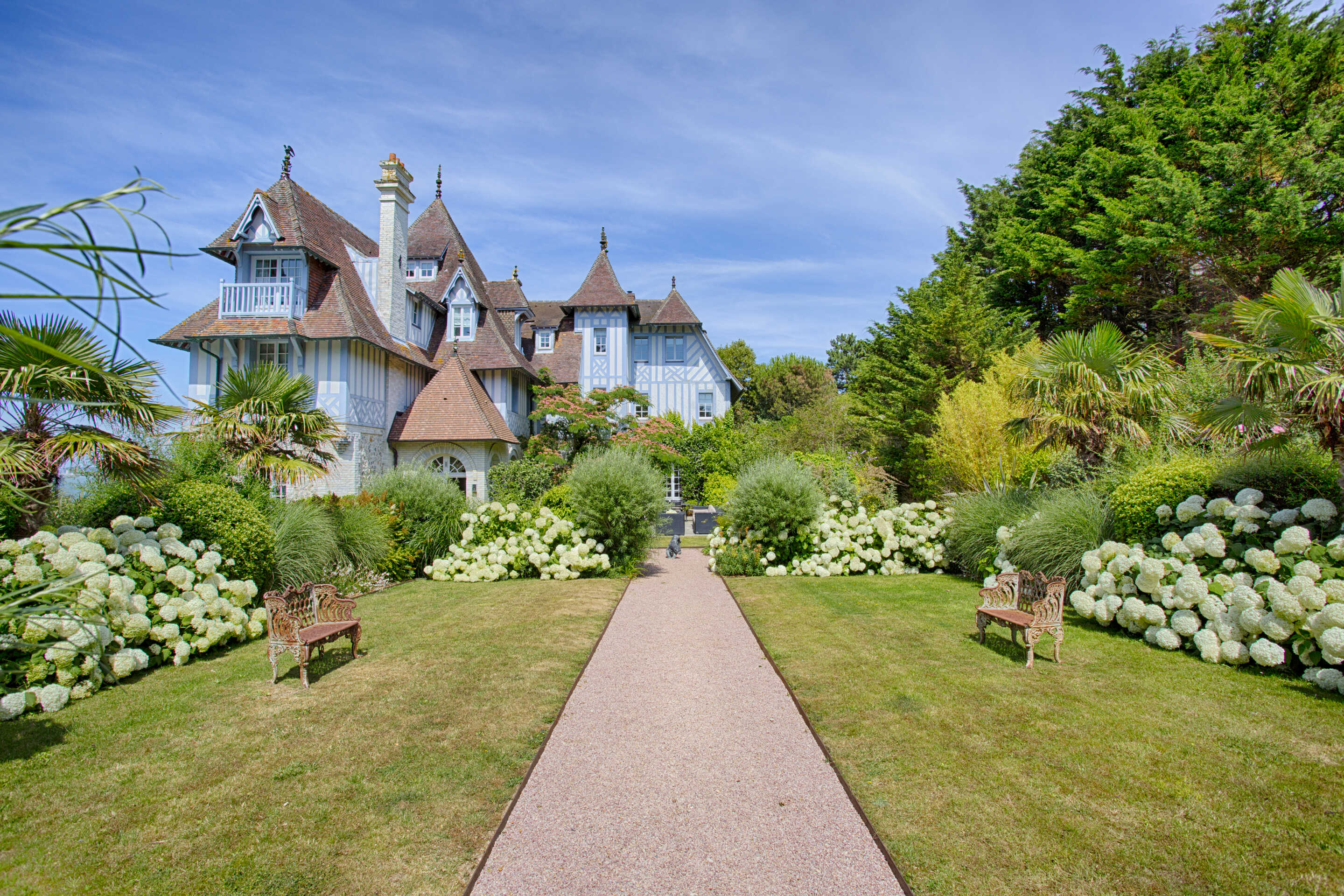 path-surrounded-with-two-wooden-benches-and-greenery-leading-to-a-manor-house-with-blue-walls